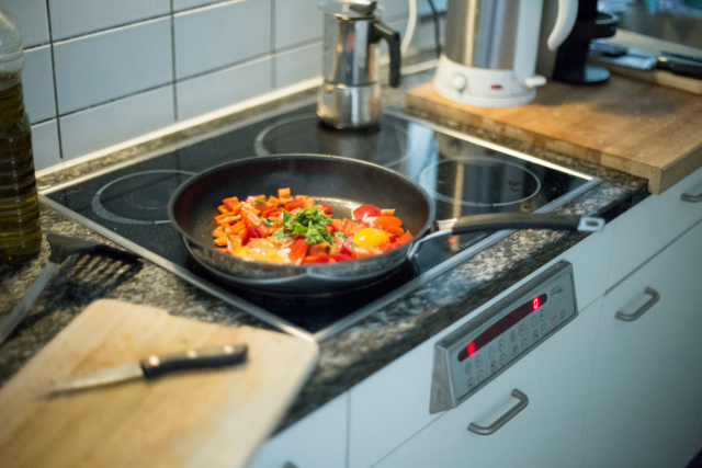 Bucătărie mică și ordonată, cu o tigaie pe aragaz și câteva ingrediente proaspete pe blat
