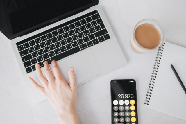 Caiet deschis cu cheltuieli notate, un calculator și o cană de cafea pe un birou
